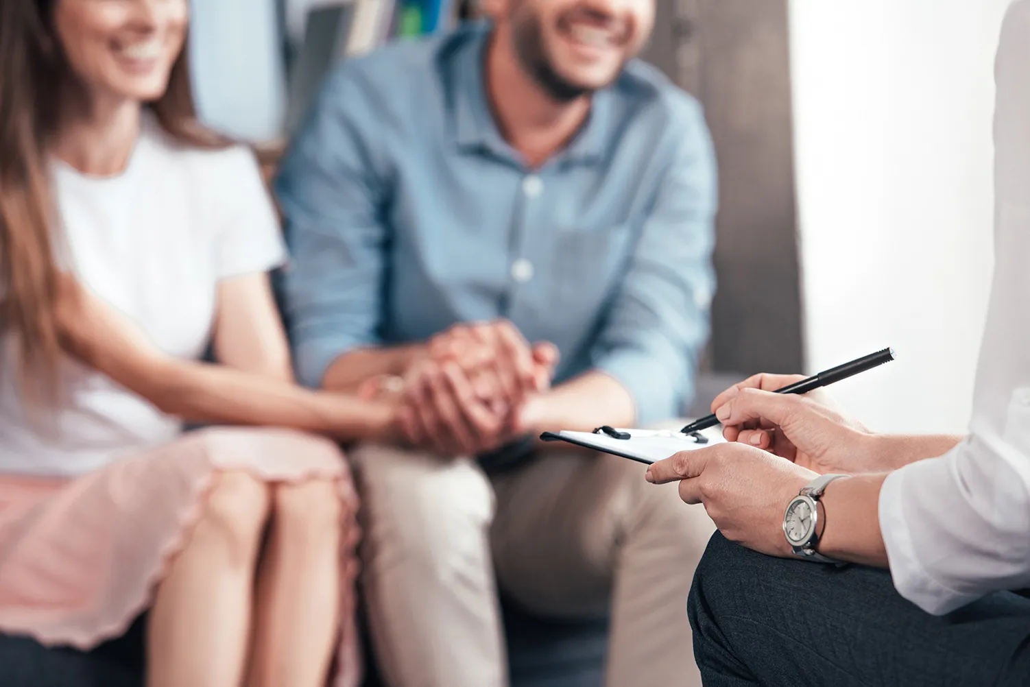 Burow Finance – Consulting GmbH – Ausschnitt aus einem Bild, auf dem eine Beraterin in ein Notizblock schreibt, während ein Paar im Büro auf dem Sofa sitzt und sich an den Händen hält